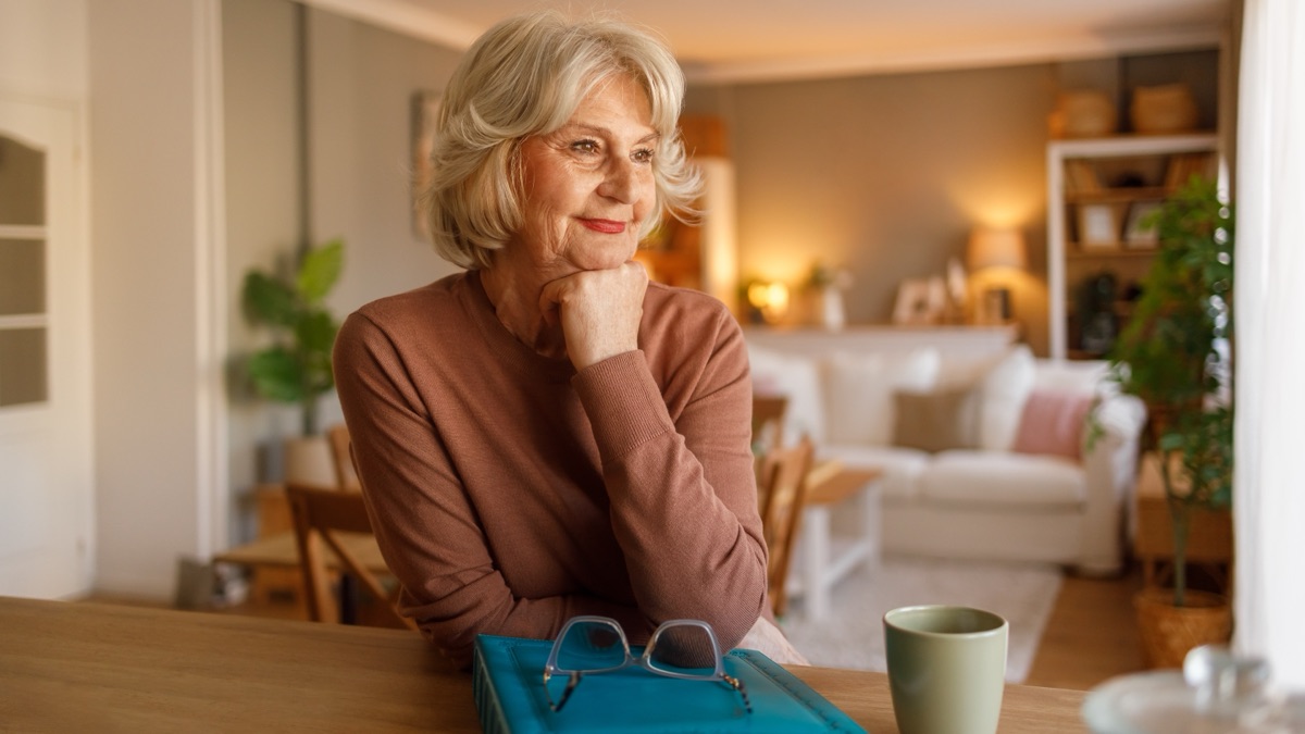 Seniorin sitzt mit Fotoalbum und Kaffeetasse am Tisch und erinnert sich an ihr Leben